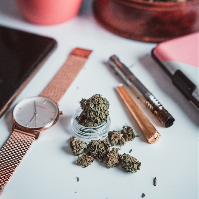cannabis and pipe on a table next to a watch